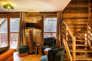 Interior de uma cabana de madeira com escadas, um sofá, uma poltrona e uma mesa.