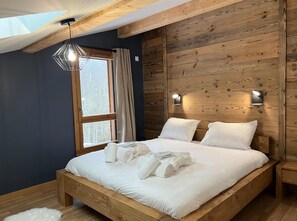Uma cama de madeira com lençóis e toalhas brancas, um claraboia e uma janela com cortinas.