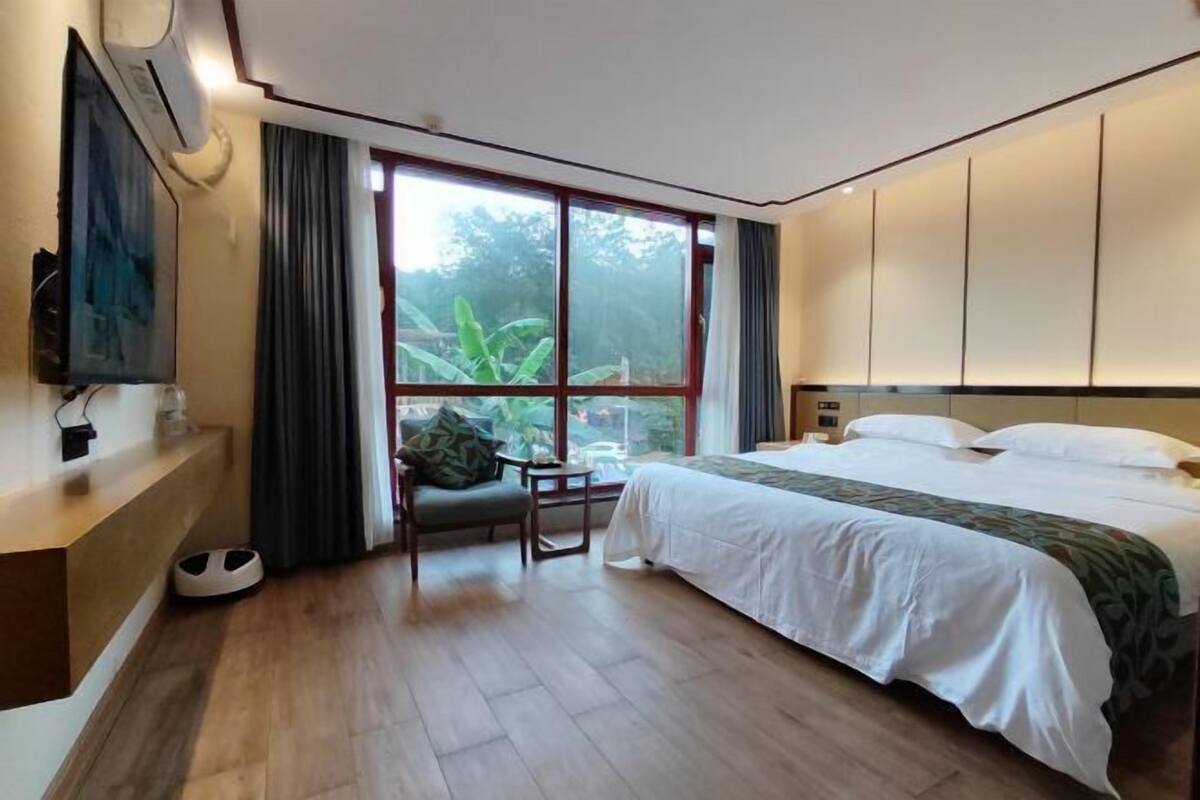 A hotel room with a large window, a bed, a desk, and a chair.