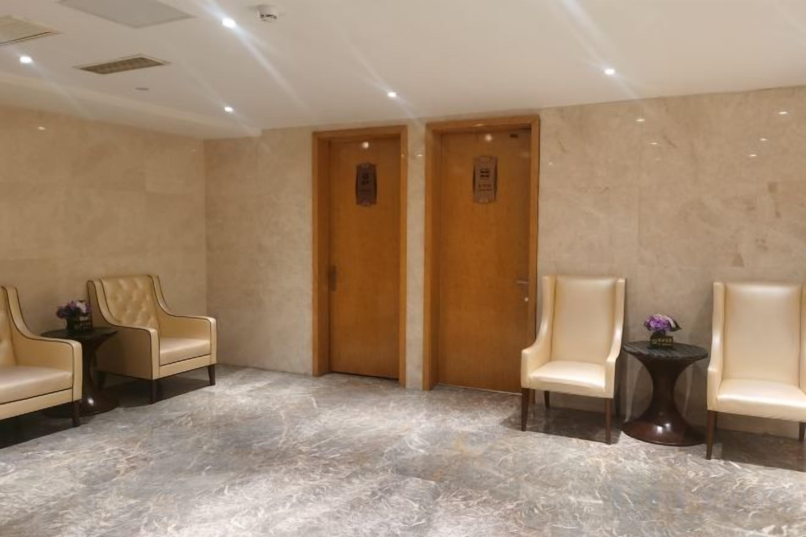 Un vestíbulo con dos puertas de madera, piso de mármol y dos sillones de cuero con una pequeña mesa en medio.