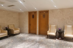Un vestíbulo con dos puertas de madera, piso de mármol y dos sillones de cuero con una pequeña mesa en medio.
