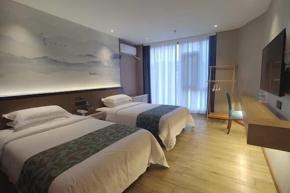 A hotel room with two beds, a large painting on the wall, a TV, and a desk with a chair.