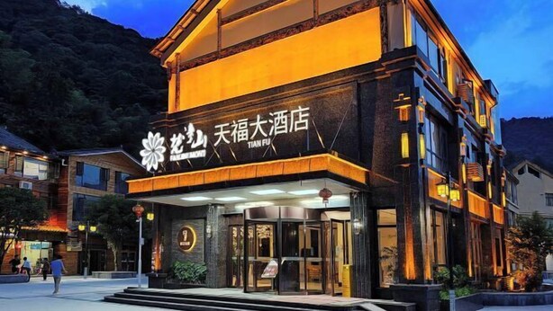 Un hôtel reconnaissable à son enseigne bien visible, écrite en caractères chinois, doté d’une architecture traditionnelle avec une façade sombre et une entrée illuminée, et d’un escalier menant à l’entrée principale.