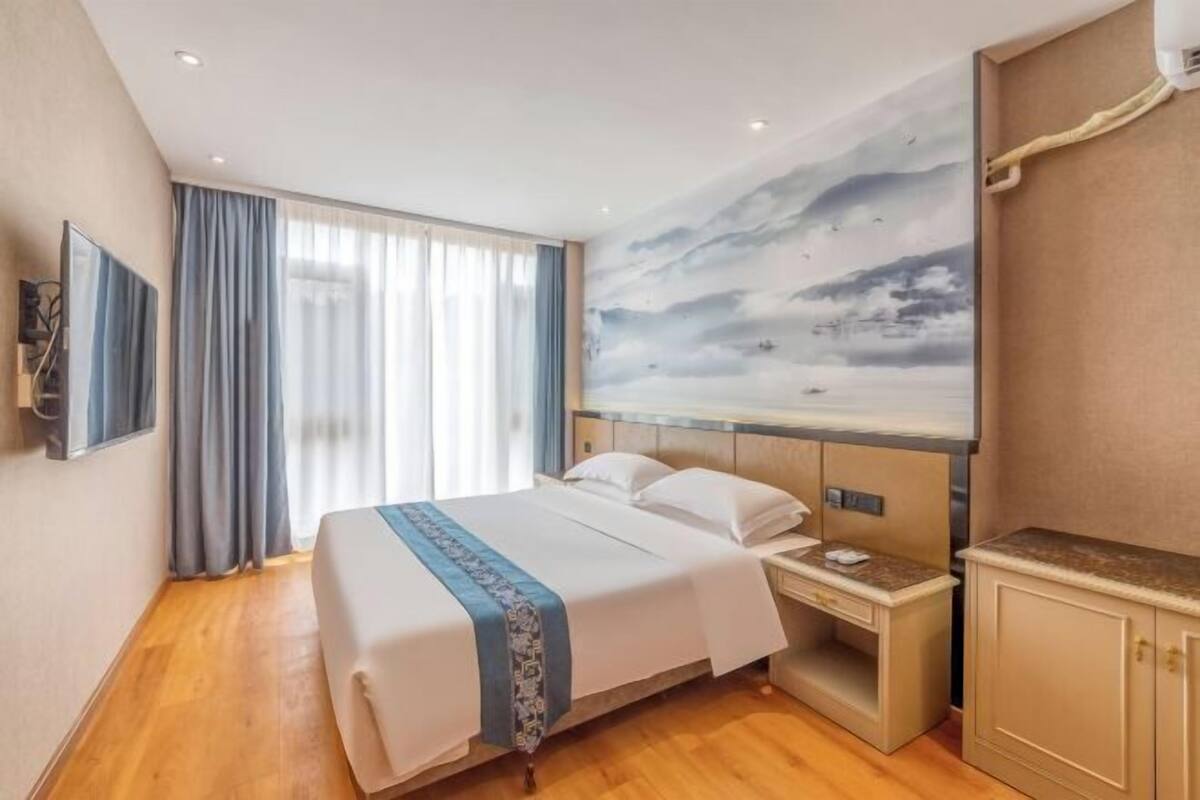 A hotel room with a large bed, a nightstand, a wardrobe, and a mural on the wall.