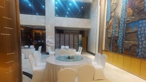 Une salle de conférence avec des tables rondes et des chaises blanches, une grande fresque murale et un plafond haut agrémenté de luminaires.