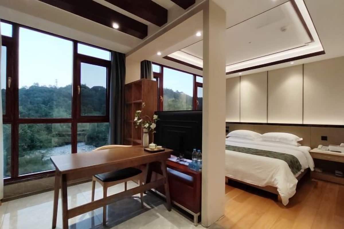 A hotel room with a bed, a desk, and a large window offering a view of the outdoors.