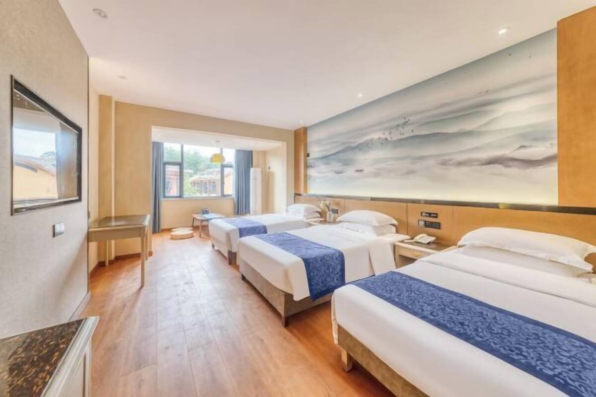 A hotel room with three beds, a large painting on the wall, and a view of the outside.