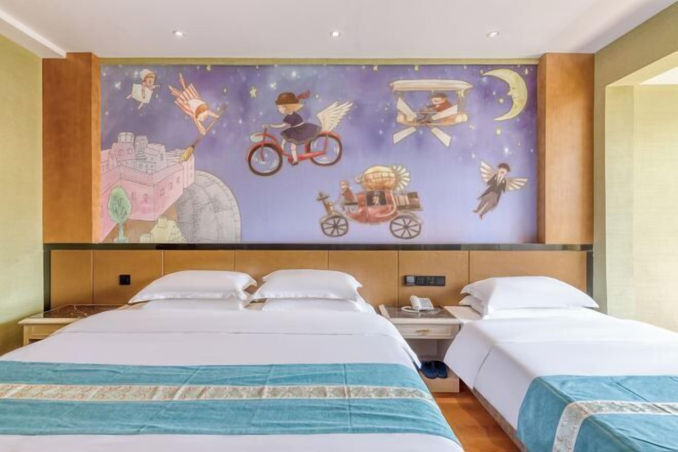 Quarto de hotel com um grande mural na parede retratando cenas fantásticas, duas camas com roupa branca e uma mesa de cabeceira com telefone.