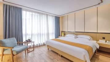 Et hotelværelse med en stor seng, en træstol, et lille bord med en lampe og et natbord med en telefon.