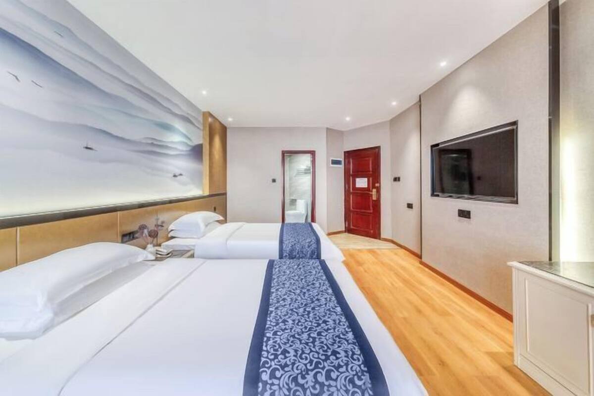 A hotel room with two beds, a large wall mural, a TV, and a wooden floor.