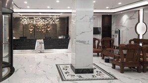 Un hall d’entrée moderne avec un sol en marbre, un comptoir d’accueil, une grande colonne et des chaises en bois.