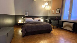 Un dormitorio con cama, mesitas de noche, radiador y ventana con persianas.