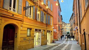 Una calle estrecha flanqueada por edificios históricos, destacando un edificio amarillo con un amplio arco de entrada y una tienda con fachada de vidrio.