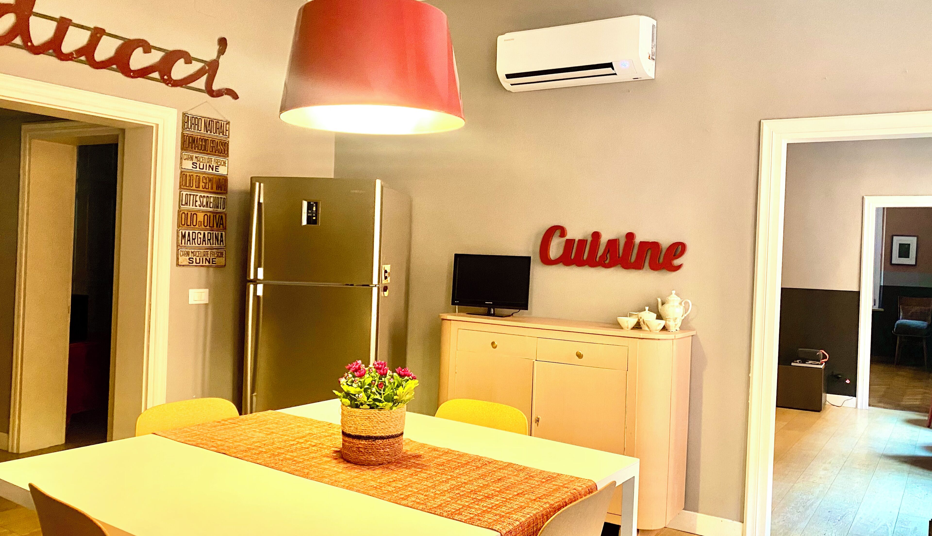 Una cocina moderna con un refrigerador de acero inoxidable, una mesa de comedor con un mantel tejido y una lámpara colgante roja.