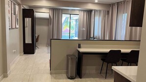 A modern hotel room with a large window, a desk, two chairs, and a trash bin.