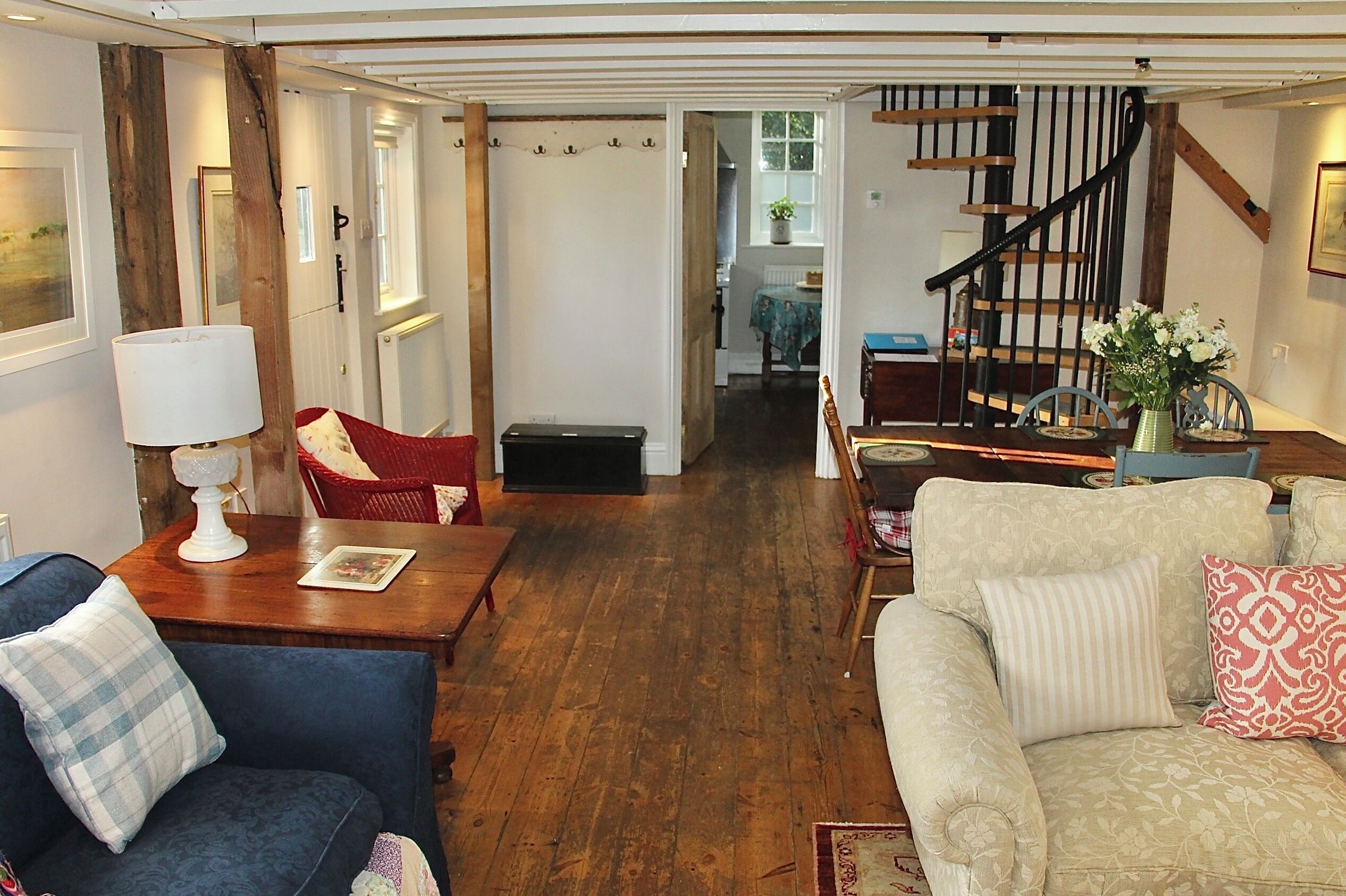 A spacious living room with a wooden floor, a staircase, and a view into another room.
