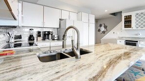 A modern kitchen with white cabinets, a stainless steel sink, and a marble countertop. - TideWatch-Relax in Brigantine w/Views,Beach and Pool (Brigantine)