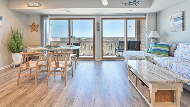A spacious living area with a balcony, a dining table with chairs, a sofa, and a ceiling fan. - TideWatch-Relax in Brigantine w/Views,Beach and Pool (Brigantine)