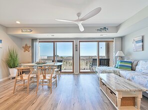 A spacious living area with a balcony, a dining table with chairs, a sofa, and a ceiling fan. - TideWatch | Brigantine Views, Beach & Pool (Brigantine)