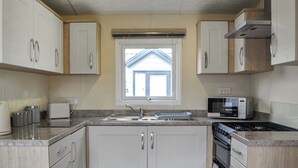 A compact kitchen with white cabinets, a built-in microwave, and a stove. - 3 bedroom accommodation in Carnaby, near Bridlington (Carnaby, near Bridlington)