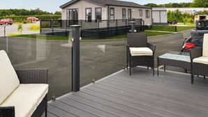 A deck with outdoor furniture, a building with a grey facade, and a parking area with cars. - 3 bedroom accommodation in Carnaby, near Bridlington (Carnaby, near Bridlington)