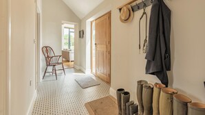 A hallway with patterned flooring, a wooden door, a chair, a coat rack with hats and a jacket, and boots. - 4 bedroom accommodation in Middlezoy, near Bridgwater (Middlezoy, near Bridgwater)