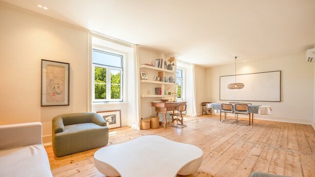 Ein geräumiges Wohnzimmer mit Holzboden, einem weißen Couchtisch, einem grauen Sofa und einem Essbereich mit Holztisch und Stühlen.
