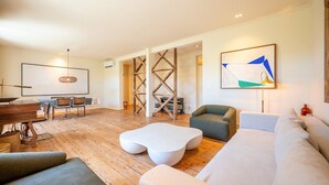 Ein geräumiges Wohnzimmer mit Holzboden, einem Essbereich mit Tisch und Stühlen, einer Treppe und einem großen abstrakten Gemälde an der Wand.