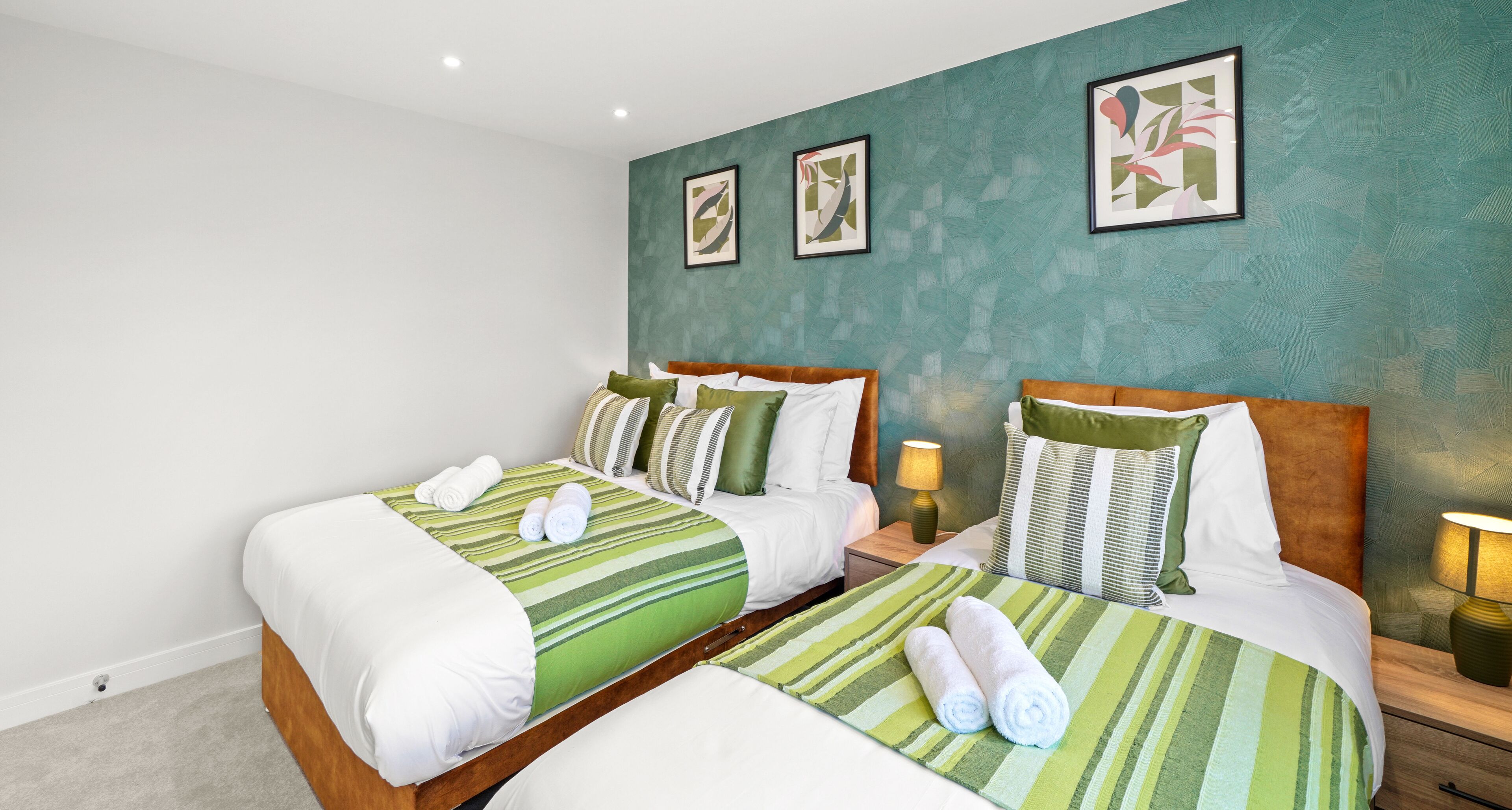 A hotel room with two beds, green striped bedding, and artwork on the walls.