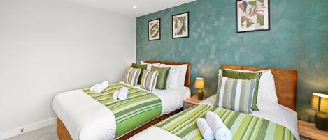 A hotel room with two beds, green striped bedding, and artwork on the walls.