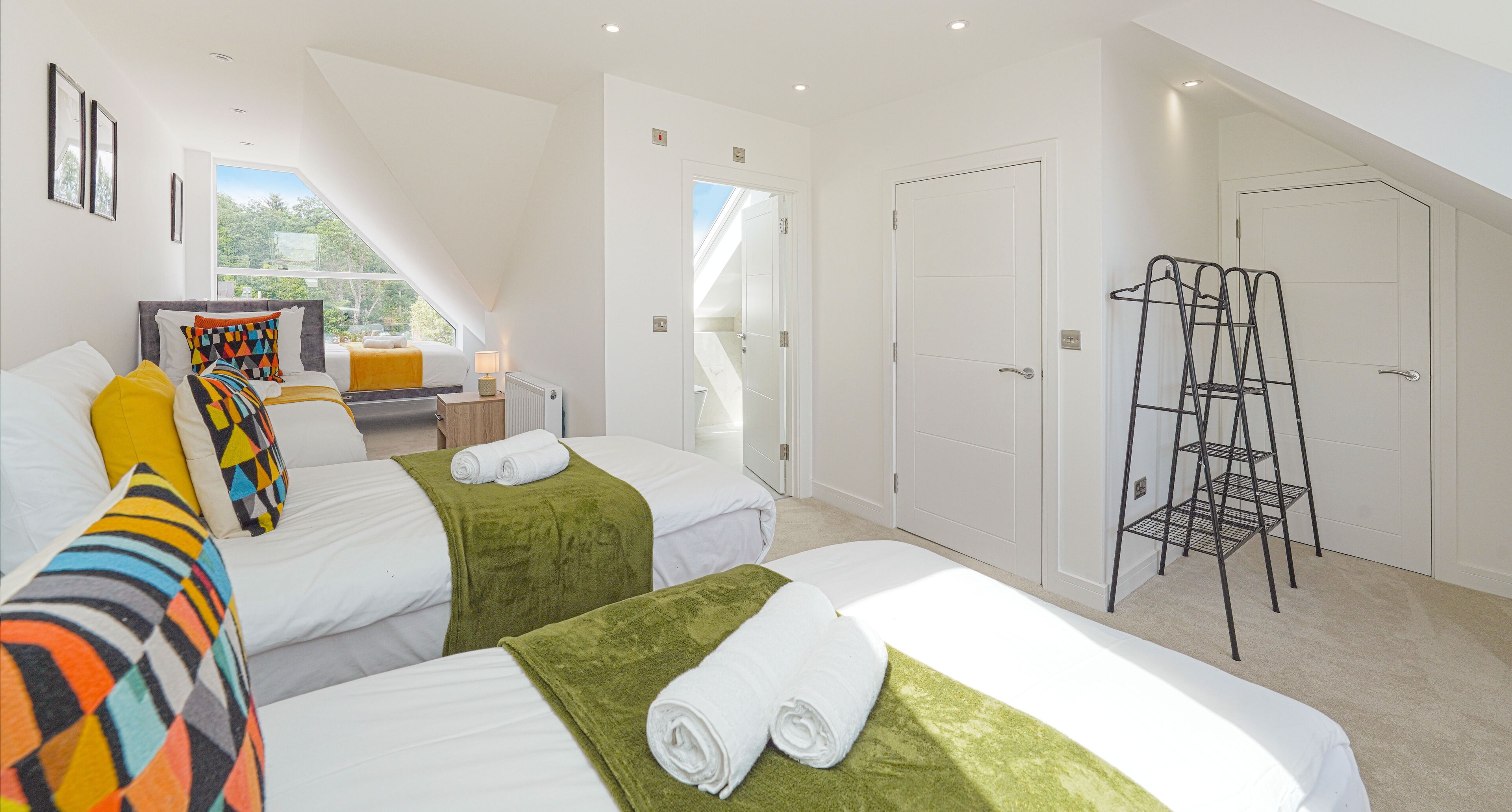A hotel room with two beds, a ladder, a desk with a lamp, and a view of the outdoors.