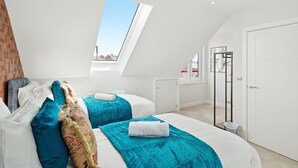 A modern bedroom with two beds, a skylight, a wardrobe, and a view of the city. - Cove Road Houses by Redwood Stays (Farnborough)