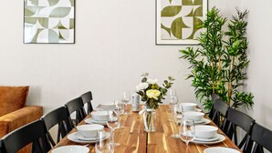 A dining table set with white plates, bowls, and wine glasses, flanked by black chairs. A vase with white flowers is placed in the center. - Cove Road Houses by Redwood Stays (Farnborough)