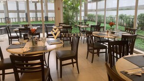 A restaurant with multiple tables and chairs, large windows, and a view of greenery outside. - Elegance Suítes Jardins (São Paulo)