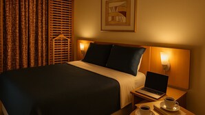 A hotel room with a bed, a laptop, and two cups of coffee on a nightstand. - Elegance Suítes Jardins (São Paulo)