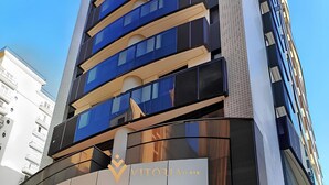 A modern building with a prominent entrance, large glass windows, and a sign reading "VITORIA." - Elegance Suítes Jardins (São Paulo)