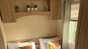Une chambre compacte dans un camping-car, équipée de deux lits, chacun agrémenté d’un plaid marron, de draps blancs et d’une petite table de chevet.