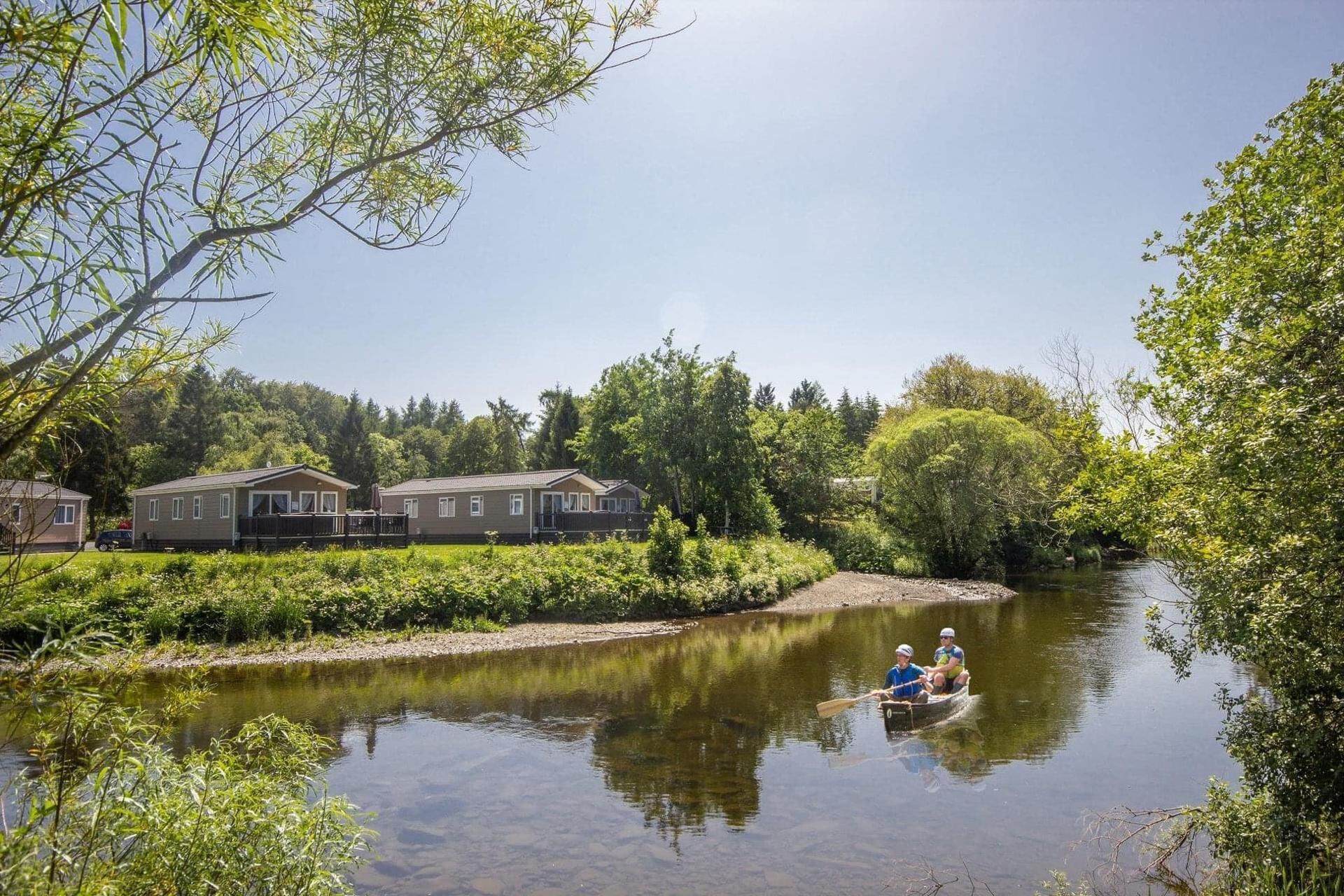 A river with a rowboat, surrounded by greenery and houses.
