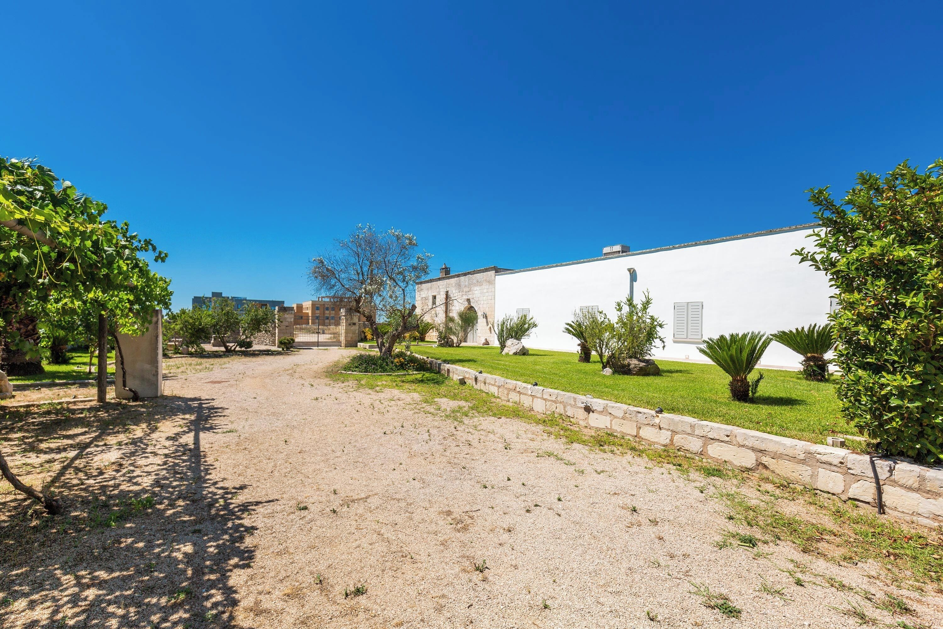A courtyard with a gravel path, a white building, and green landscaping.