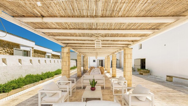An outdoor seating area with white furniture, a bamboo ceiling, and a stone wall. - Agriresort Masseria Giovanni - Tripla (Martano)