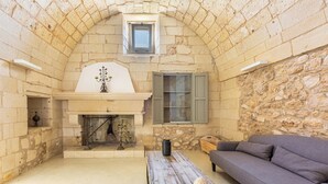 A stone-walled room with a fireplace, a sofa, and a wooden table. - Agriresort Masseria Giovanni - Tripla (Martano)