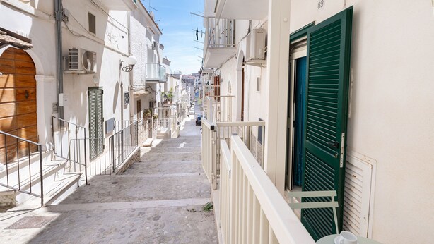 Eine enge Straße mit Gebäuden an beiden Seiten, ein Balkon mit gedecktem Tisch und einem klaren Himmel.