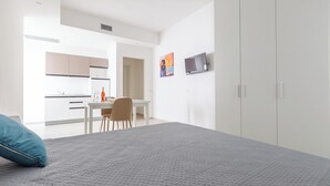 Ein modernes Schlafzimmer mit einem großen Bett, einem Schreibtisch und einer kleinen Küche im Hintergrund.