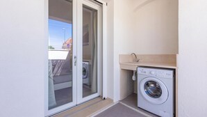 Lavanderia con lavatrice e lavandino, adiacente a una porta scorrevole in vetro che dà su un balcone.