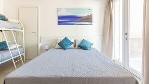 Una stanza con un letto a castello, un grande letto con cuscini, un quadro raffigurante un faro e una porta finestra.