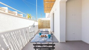 Un balcone con un tavolo apparecchiato per due, un pergolato in legno e un muro bianco.
