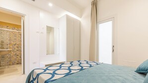 A bedroom with a bed, a wardrobe, a mirror, and a bathroom with a shower and sink. - Residence Albeach - Bilo 3 (Porto Cesareo)