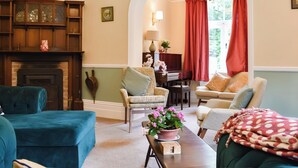 A cozy living room with a fireplace, comfortable seating, and a piano. - 6 bedroom accommodation in Okehampton (Okehampton)