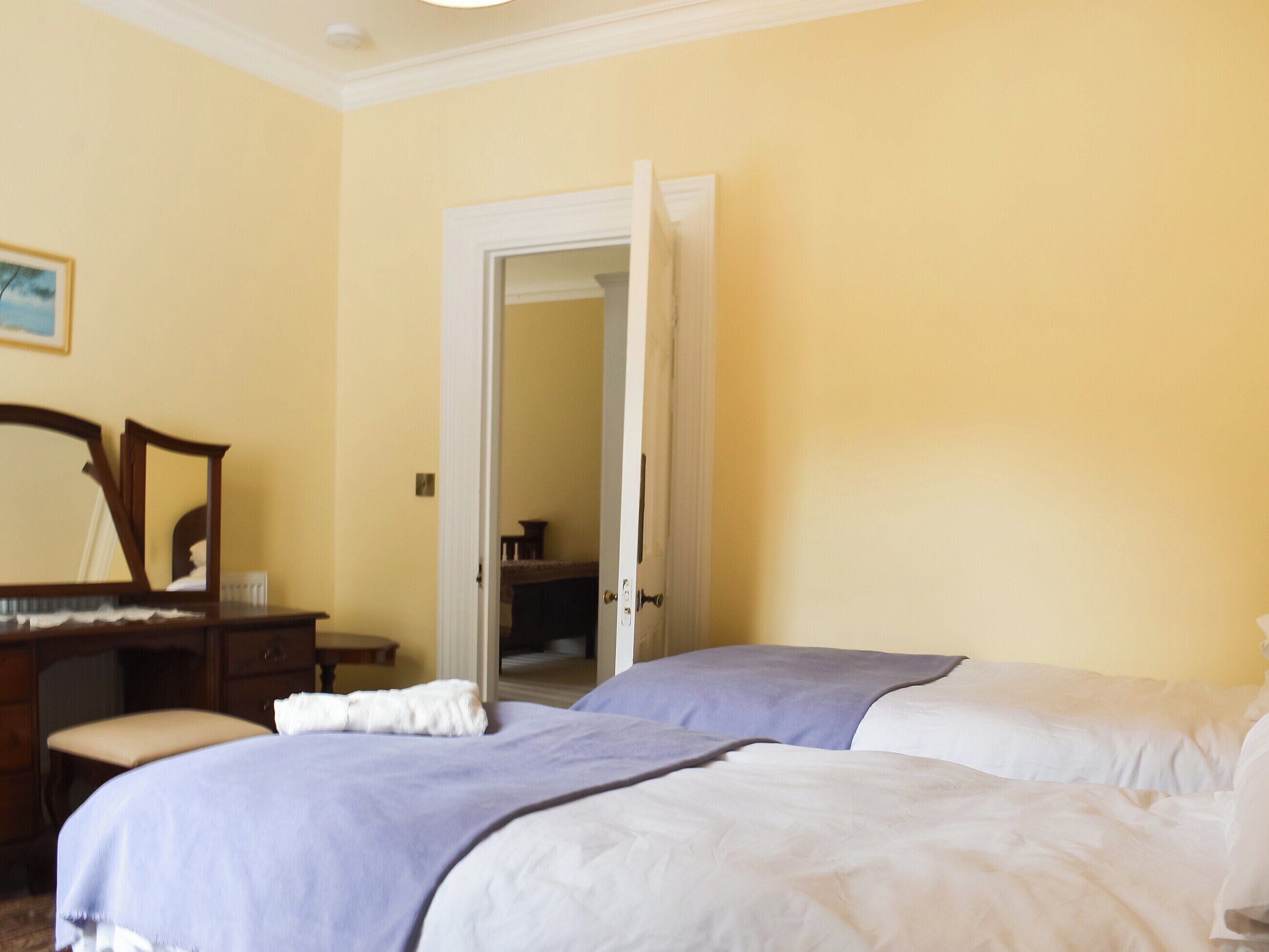 A hotel room with two beds, a wooden dresser, a mirror, and a door leading to another room.