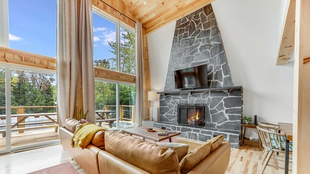 Una sala de estar acogedora con chimenea de piedra, sofá de cuero y ventanas amplias con vistas a una terraza.
